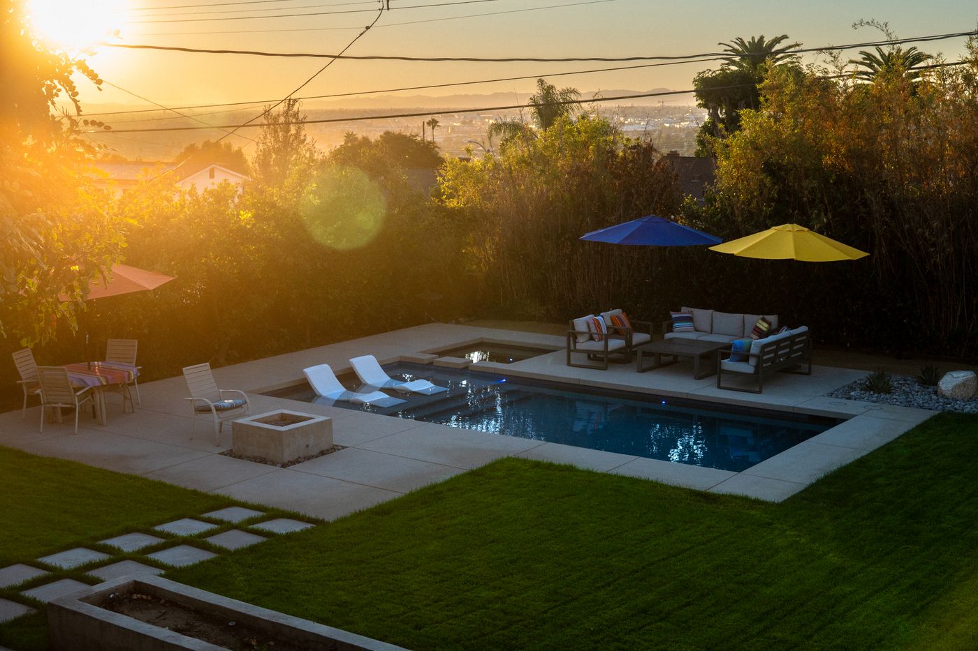 Dated backyard with a red brick patio and fire pit, exposed irrigation tubing, and a plain lawn overlooking a hillside view, prior to renovation